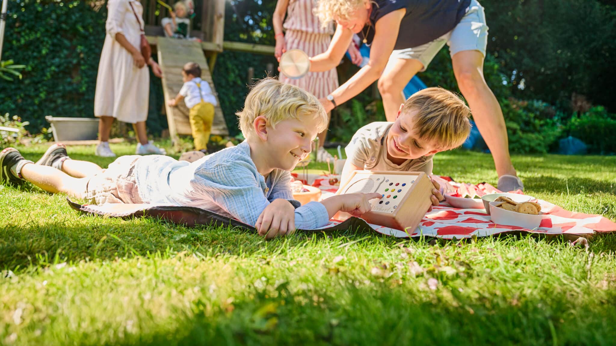 Deux garçons écoutent hörbert sur la couverture de pique-nique, pendant que d'autres enfants jouent en arrière-plan