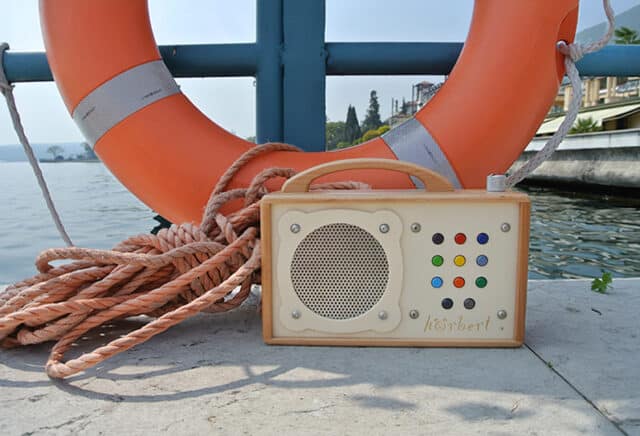 Sur cette image, on voit un lecteur de musique hörbert avec 9 playlists, posé sur un ponton d'un plan d'eau. À l'arrière-plan, on aperçoit une bouée de sauvetage à rayures orange et blanches ainsi que des cordages.